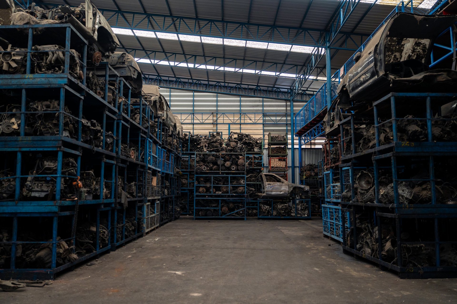Large industrial warehouse filled with stacked metal shelves containing used automotive parts, engines, and vehicle components for recycling