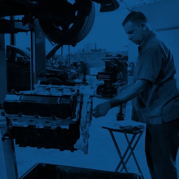 Mechanic working on a car engine in a garage workshop with blue lighting and tools visible in background